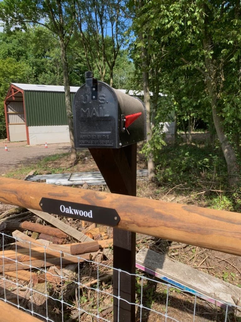 Black post box with a red flag at Keep Safe Storage stands outside a storage barn with a sign reading Oakwood underneath.